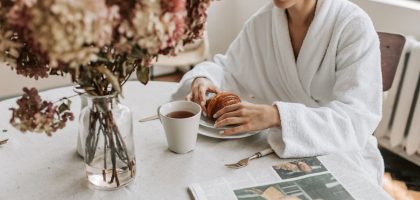 A woman in a bathrobe having breakfast indoors with a croissant and tea.
