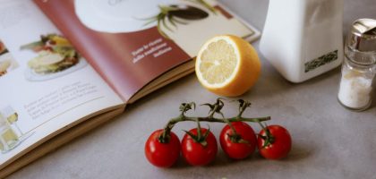 Flat lay of cooking ingredients including tomatoes and a lemon with a cookbook.