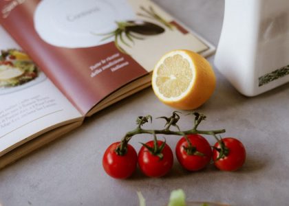 Flat lay of cooking ingredients including tomatoes and a lemon with a cookbook.